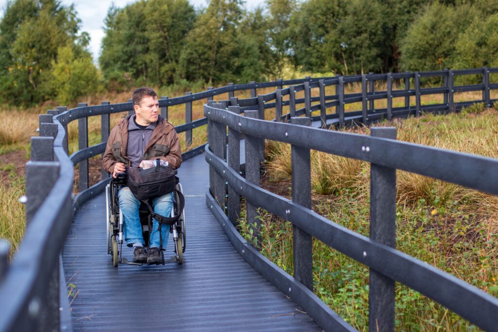 Man in wheelchair on a boardwalk in a wooded outdoor setting