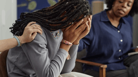African American teenage girl covering face with hand showing distress in support group therapy session