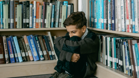 Male student huddled in a corner of a library looking upset