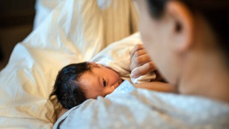 Mother breastfeeding newborn baby in hospital ward, first breastfeeding
