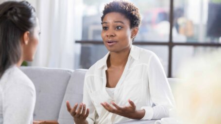 Young African American woman gestures while talking with a female therapist. The patient has a concerned expression on her face.